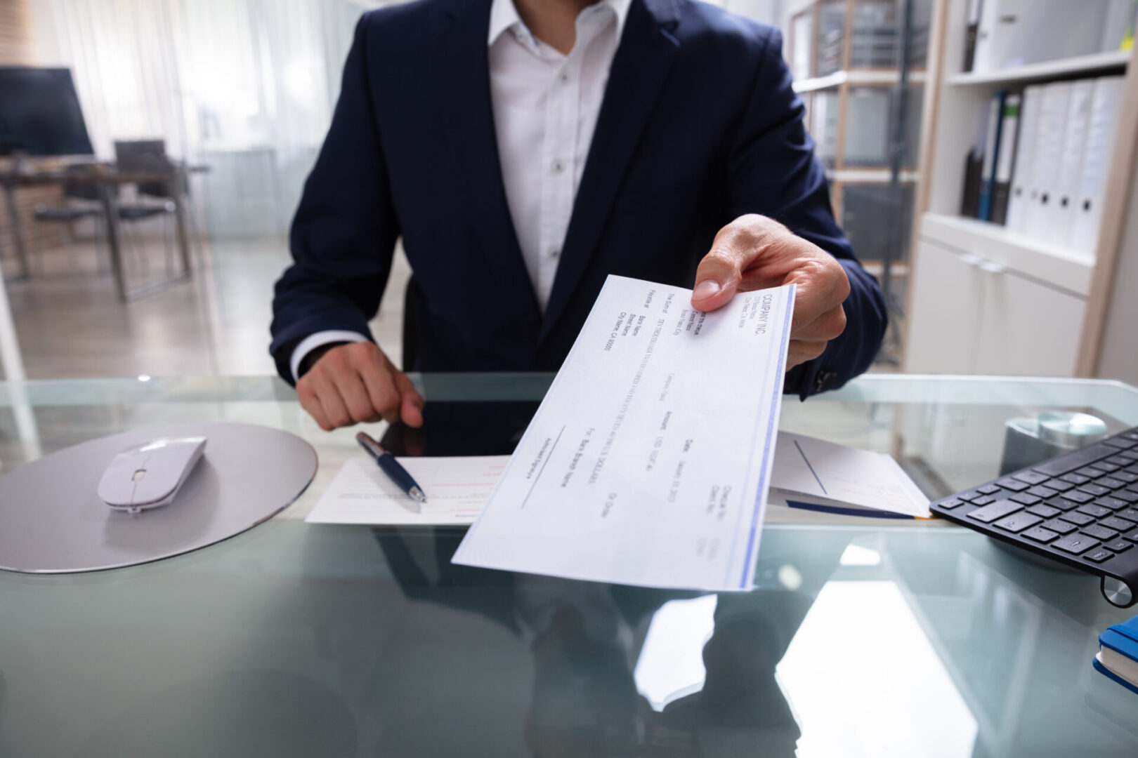 Businessman Giving Cheque Businessman's Hand Giving Cheque Over Glass Desk